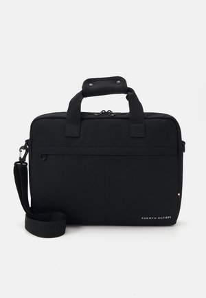 Mallette rectangulaire noire avec poignées sur le dessus, bandoulière, fermeture éclair et petit logo Tommy Hilfiger en bas à droite.