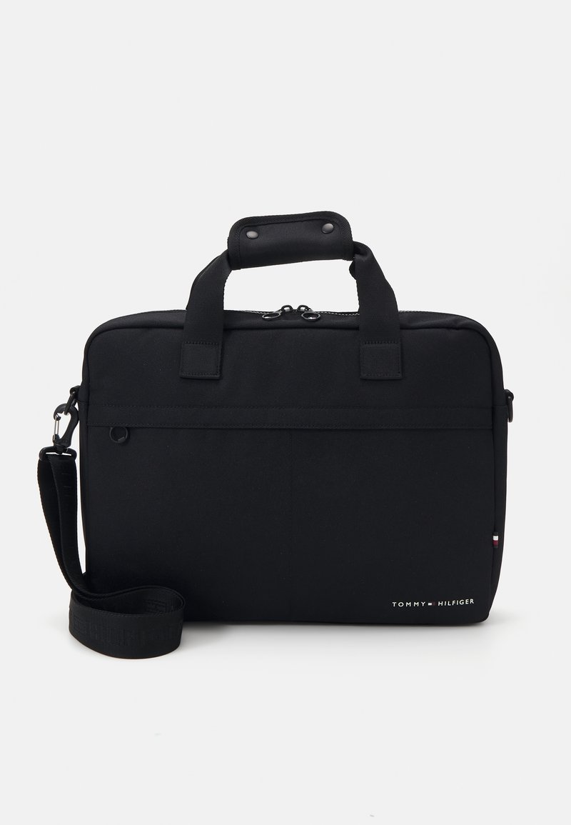 Mallette rectangulaire noire avec poignées sur le dessus, bandoulière, fermeture éclair et petit logo Tommy Hilfiger en bas à droite.