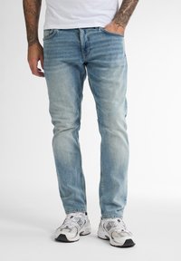 Vaqueros de mezclilla azul claro con corte recto, cinco bolsillos, un ligero desvanecimiento y detalles de costura, combinados con zapatillas blancas.