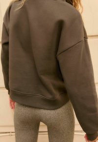 Olijfgroene sweatshirt met een relaxte pasvorm en ingezakte schouders, gecombineerd met gestructureerde grijze leggings. Zachte stof, geribbelde manchetten en zoom.