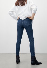 Slim fit jeans i mörkblå denim med en klassisk femfickdesign och en slät yta. Kombineras med svarta ankelstövlar.