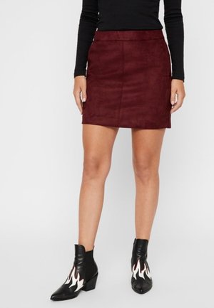 Jupe mini en suédine bordeaux avec une texture lisse et une silhouette ajustée, associée à des bottines noires avec des accents de flammes blanches.