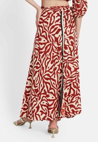 Falda maxi en rojo y crema con un patrón floral. Cuenta con un cierre de cremallera en la parte posterior. Fabricada con un tejido ligero y de textura suave.