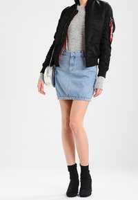 Veste bomber noire, pull gris, jupe en denim bleu clair avec un ourlet effiloché, et bottines noires avec une touche bleue. Sac à main avec des détails scintillants.