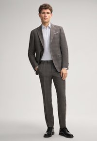 Costume à carreaux gris avec une coupe ajustée ; veste à un bouton et pantalon assorti. Associé à une chemise claire et des chaussures de ville noires.