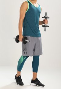 Tyrkis linne med neongröna detaljer, grå shorts med sidopaneldesign, teal leggings och svarta träningsskor, håller vikter.