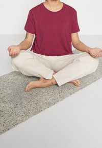 Camiseta de algodón burdeos y pantalones crema texturizados, usados en una posición de meditación sentada sobre una estera gris salpicada.