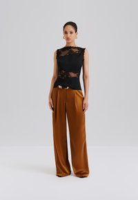 Top negru fara maneci cu detalii din dantelă, asortat cu pantaloni largi, cu talie înaltă, din satin, într-o nuanță caldă de maro, cu o curea vizibilă.