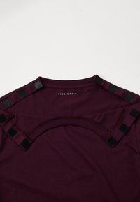 Bordó póló kerek nyakkivágással és fekete részletekkel, textúrált felülettel a vállakon. A hátsó részen látható a "PIER ONE" címke.