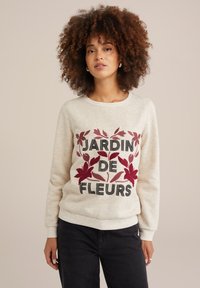 Kremeni sweatshirt s natpisom "JARDIN DE FLEURS", ukrašen maroon cvjetnim grafikama. Rebrasti rukavi i rub, mekana tekstura tkanine.