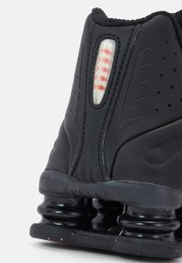 Black athletic shoe with a synthetic upper, padded collar, and distinctive spring-style sole. Features red detailing and ventilation holes.