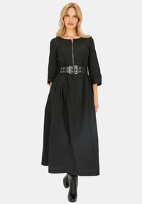 Czarna sukienka z długim rękawem, z zamkiem z przodu, z dopasowaną talią za pomocą szerokiego paska z okrągłymi oczkami i zwiewnym dołem. Gładka tekstura.