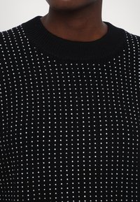 Pull en tricot noir avec des côtes verticales, orné de sequins argentés éparpillés et d'un col rond.