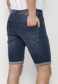 Traperice kratke hlače u tamnoplavoj boji s ravnim krojem, s preklopljenim rubovima, dva stražnja džepa i smešnim kožnim etiketom na pojasu.
