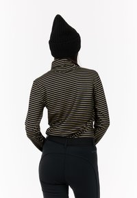 Haut à manches longues noir et or à rayures avec un col haut, associé à un pantalon noir ajusté et un bonnet noir côtelé.