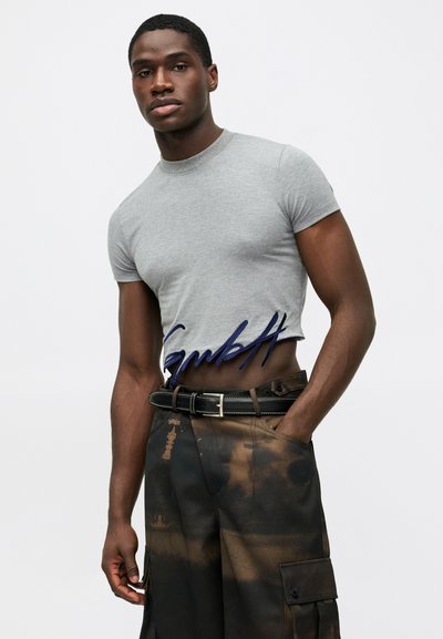 Pilkas trumpas marškinėliai su apvaliu iškirpimu, išsiuvinėtu mėlynu tekstu. Dėvimi su tamsiais, raštuotais kargo kelnėmis ir juodu diržu.