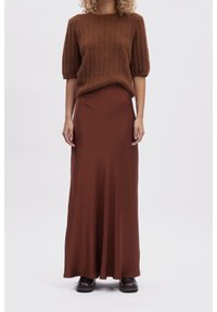 Pull court à manches courtes marron côtelé associé à une longue jupe fluide marron en tissu lisse. La modèle porte des bottines noires.
