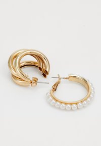 Brincos de ouro em forma de argola, apresentando três anéis interligados à esquerda e uma única argola adornada com pequenas pérolas brancas à direita.