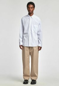 Koszula w paski w kolorze białym i jasnoniebieskim, z zapięciem na guziki z przodu, kołnierzykiem i kieszenią na piersi. Do tego beżowe spodnie o szerokich nogawkach i czarne buty.