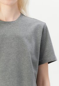 T-shirt gris à manches courtes en tissu léger et doux, avec un col rond, présentant une texture lisse et des coutures minimales.