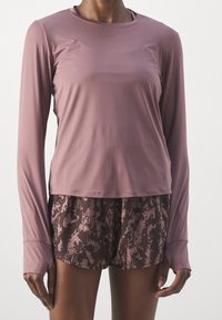 Langærmet, lyse lilla sportstop med rund hals, kombineret med mønstrede brune shorts med tekstureret design.