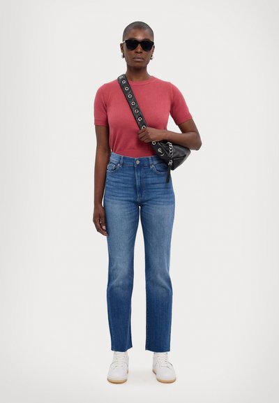 Top corto de color óxido, jeans de tiro alto azules, bolso negro bandolera con acentos metálicos, zapatillas blancas y gafas de sol negras.