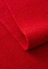 Piros kötött textil, ribbelt felszínnel, látható varrással és puha tapintással, hajtva, hogy a mélységet és a vastagságot bemutassa.