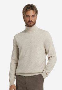 Jasno beżowy sweter typu golf w miękkiej dzianinie, charakteryzujący si�ę dopasowanym krojem, długimi rękawami oraz prążkowanymi mankietami i dolnym wykończeniem.
