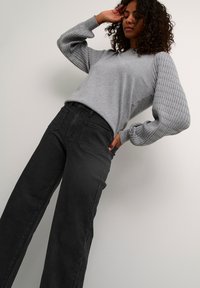 Pull gris avec des manches texturées et côtelées, associé à un jean noir à jambes larges taille haute. Design simple et décontracté avec une coupe ample.