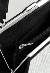 Schwarze Stoffhandtasche mit einem silbernen metallischen Verschluss, ausgestattet mit einer inneren Reißverschlusstasche und einem strukturierten Panel auf einer Seite.