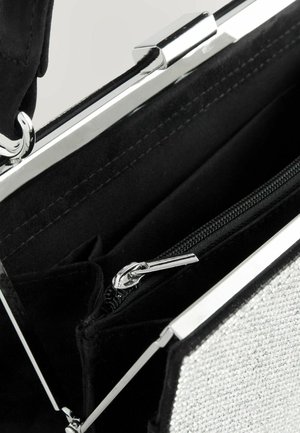 Sac à main en tissu noir avec un fermoir métallique argenté, comprenant une poche intérieure zippée et un panneau texturé sur un côté.