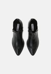 Un paio di stivaletti neri in pelle con punta appuntita e dettagli in rivetti attorno all'apertura e alla parte superiore, etichettati Steve Madden all'interno.