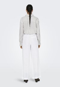 Chemise en lin rayée à coupe décontractée, associée à un pantalon en lin blanc à jambes larges. Comprend une poche arrière sur le pantalon et des manches longues.