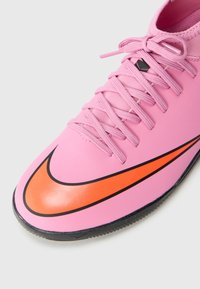 Rosa treningssko med klar oransje og svart swoosh-logo, rosa lisser og svart såle på hvit bakgrunn.