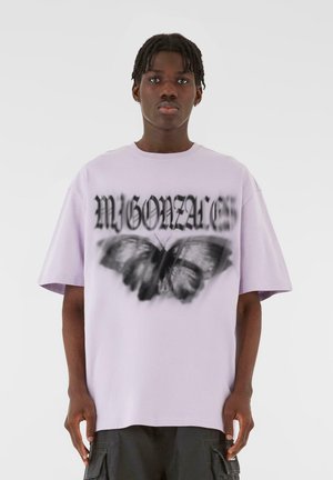 Lilla oversized t-skjorte med et svart sommerfugl grafikk og tekstdesign. Korte ermer og rund hals. Glatt stofftekstur.