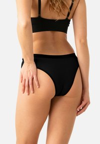 Sous-vêtement noir taille haute en tissu lisse, avec une ceinture extensible et un design minimaliste. Vue arrière montrant une couverture complète en forme incurvée.