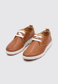 Chaussures en cuir perforé marron avec des lacets blancs, un bout arrondi et une semelle en caoutchouc blanche. Design minimaliste avec une languette arrière.