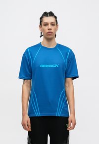 Camisa desportiva Reebok de manga curta azul com riscas e logótipo azul claro. O tecido parece suave e leve. Projetada para uso ativo.