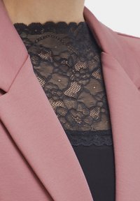 Blushfärgad kavaj i ett texturerat tyg, med ett svart spetspanel undertill. Spetsen har blommönster och vågiga kanter.