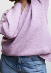 Pull en tricot doux couleur lavande avec col en V et poignets côtelés, associé à un jean en denim bleu clair, présentant une coupe décontractée et un style casual.