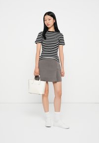 Svart og hvit striped t-skjorte, grå skjørt, hvite joggesko og liten hvit håndveske. Lett, glatt stoff med en avslappet passform.