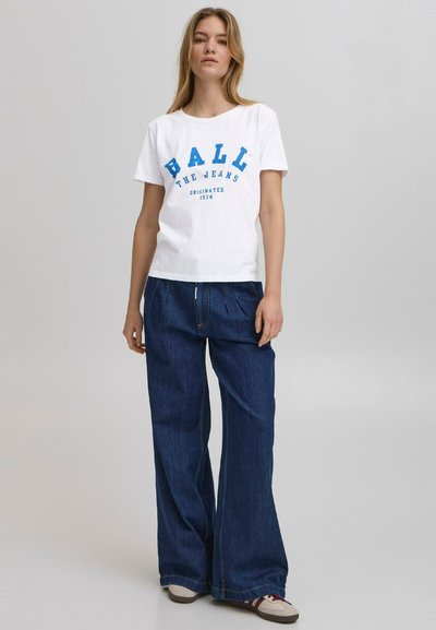 Hvit bomulls t-skjorte med blå grafisk tekst, kombinert med vide mørk denimbukser. Sneakers med beige og burgunder aksenter.
