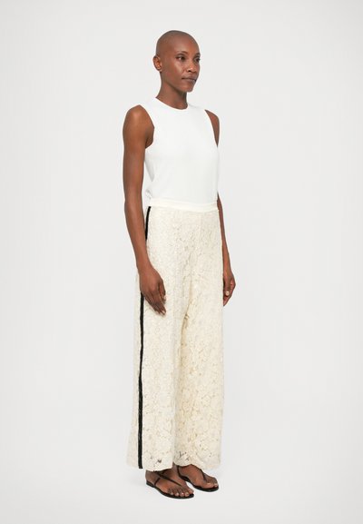 Top branco sem mangas combinado com calças largas de renda creme com uma faixa lateral preta. Tecido suave com um delicado padrão floral.
