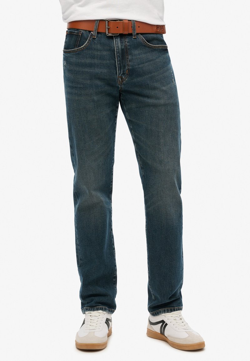 Jeans de mezclilla de color azul oscuro con corte recto, que presentan un cinturón marrón. Los jeans tienen un lavado sutil y un diseño clásico de cinco bolsillos.