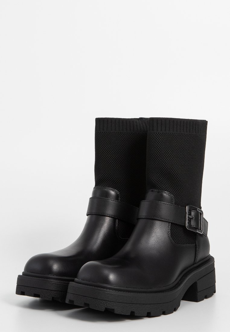Czarne botki za kostkę z gładkiej skóry, teksturowanym czarnym dzianinowym cholewką, szczegółem z boku w postaci klamry oraz masywną podeszwą z bieżnikiem.
