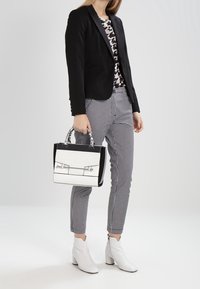 Blazer noir, top blanc à motifs, pantalon à carreaux, bottines blanches à cheville et un sac à main bicolore avec quincaillerie argentée.