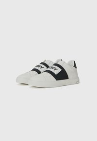 Sneaker bianchi e nere con cinturini elasticizzati, texture liscia, punta arrotondata e suola in gomma. Presentano il logo sui cinturini e un accento nero sul tallone.
