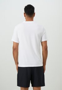 White cotton t-shirt with short sleeves, featuring a crew neck and a relaxed fit, paired with dark shorts, viewed from the back.
