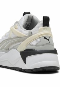 Tenisky Puma RS-X s bílou síťovinou, šedými a krémovými akcenty, silnou bílou a černou podrážkou a polstrovaným límcem kolem paty.