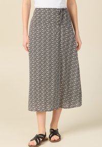Falda midi de patrón floral en blanco y negro con un ajuste holgado, tela ligera y detalle de cintura anudada. Combinada con sandalias negras de tiras.